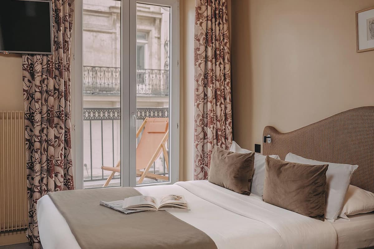 Una habitación de hotel con una cama, una silla junto a la ventana y un televisor en la pared.