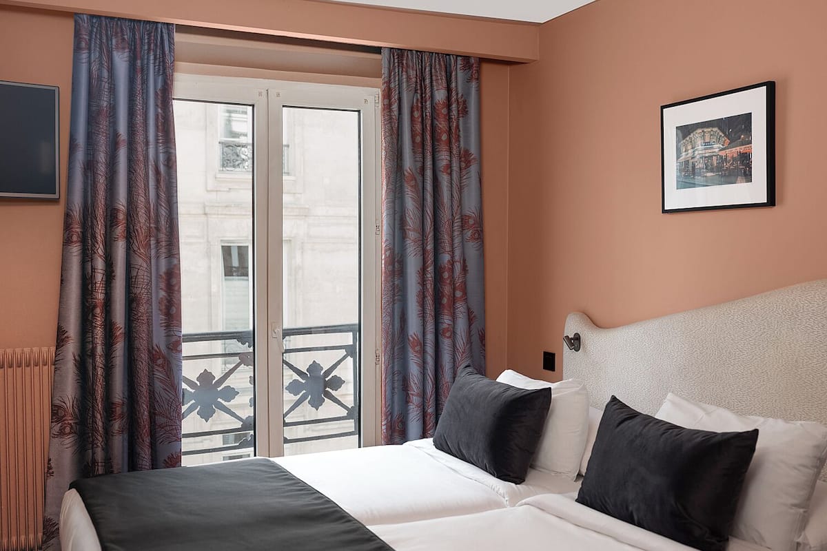 Habitación de hotel con cama, cortinas, un cuadro enmarcado y vistas por la ventana.