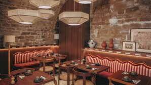 Un restaurante con mesas y bancos de madera, lámparas de mimbre colgantes y un fondo de pared de ladrillo.