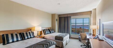 A hotel room with two beds, a desk, a chair, a TV, and a large window with a view.