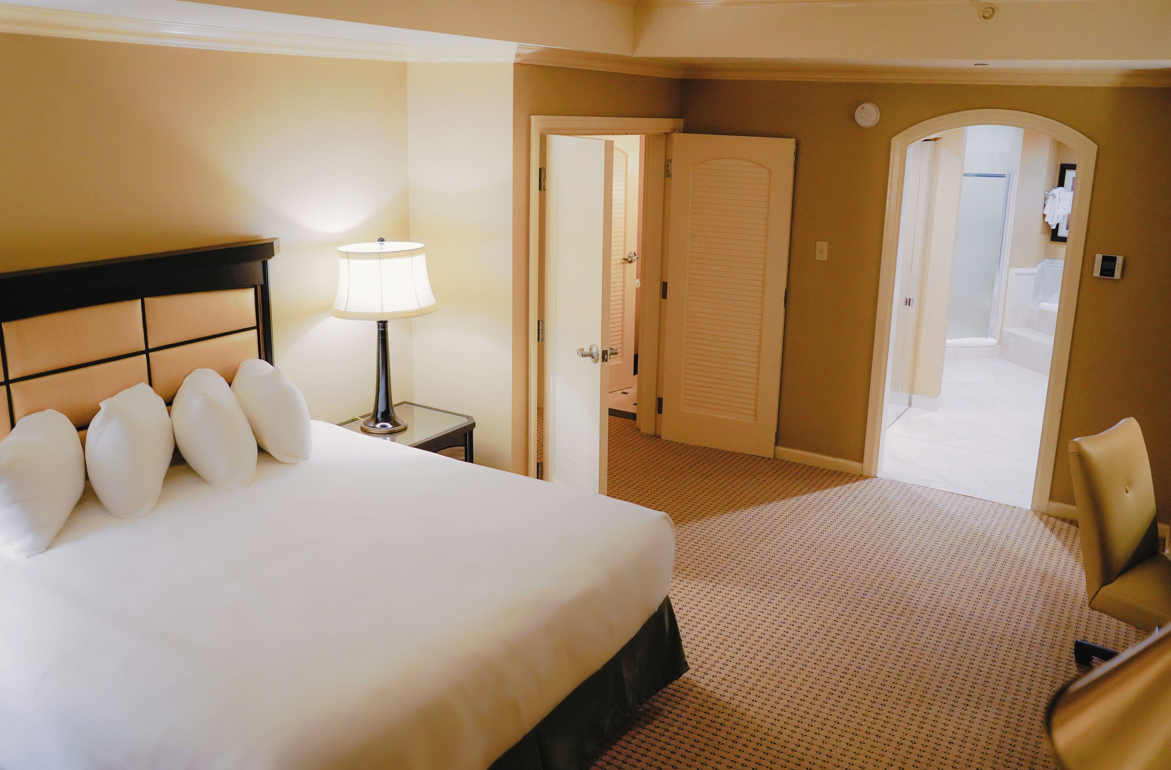 A hotel room with a bed, a nightstand, a lamp, a chair, and a door leading to a bathroom.