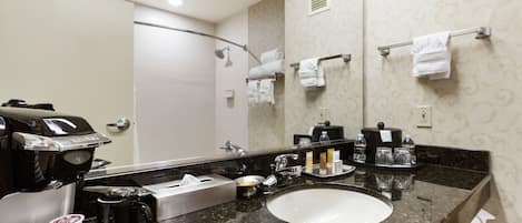 A hotel bathroom with a large mirror, a sink, a coffee maker, and towels on a rack.