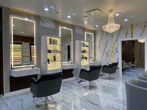 Un salón moderno con suelos de mármol, espejos grandes y sillones de peluquería negros.