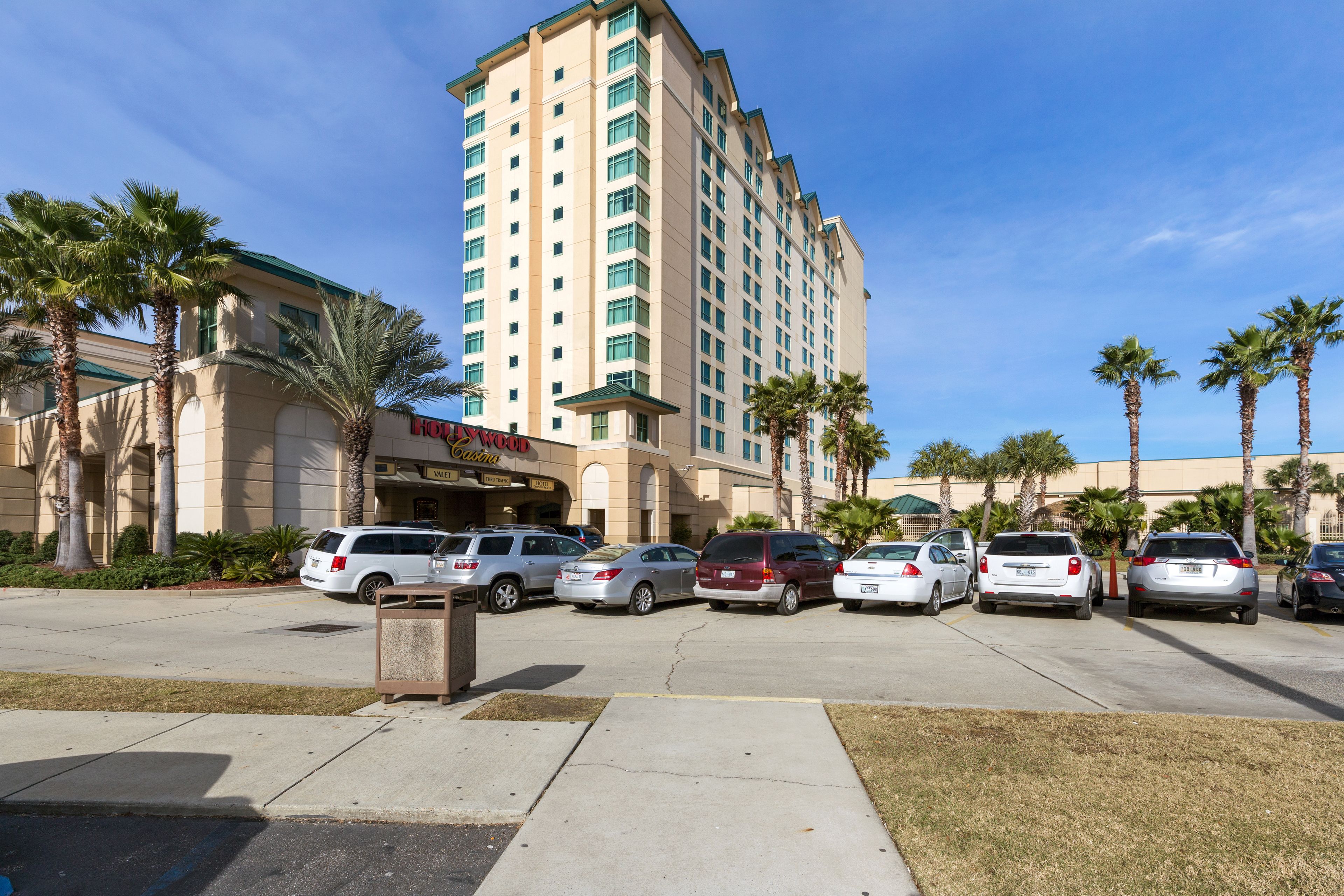 A hotel with a modern design, featuring a parking lot with several cars and palm trees.