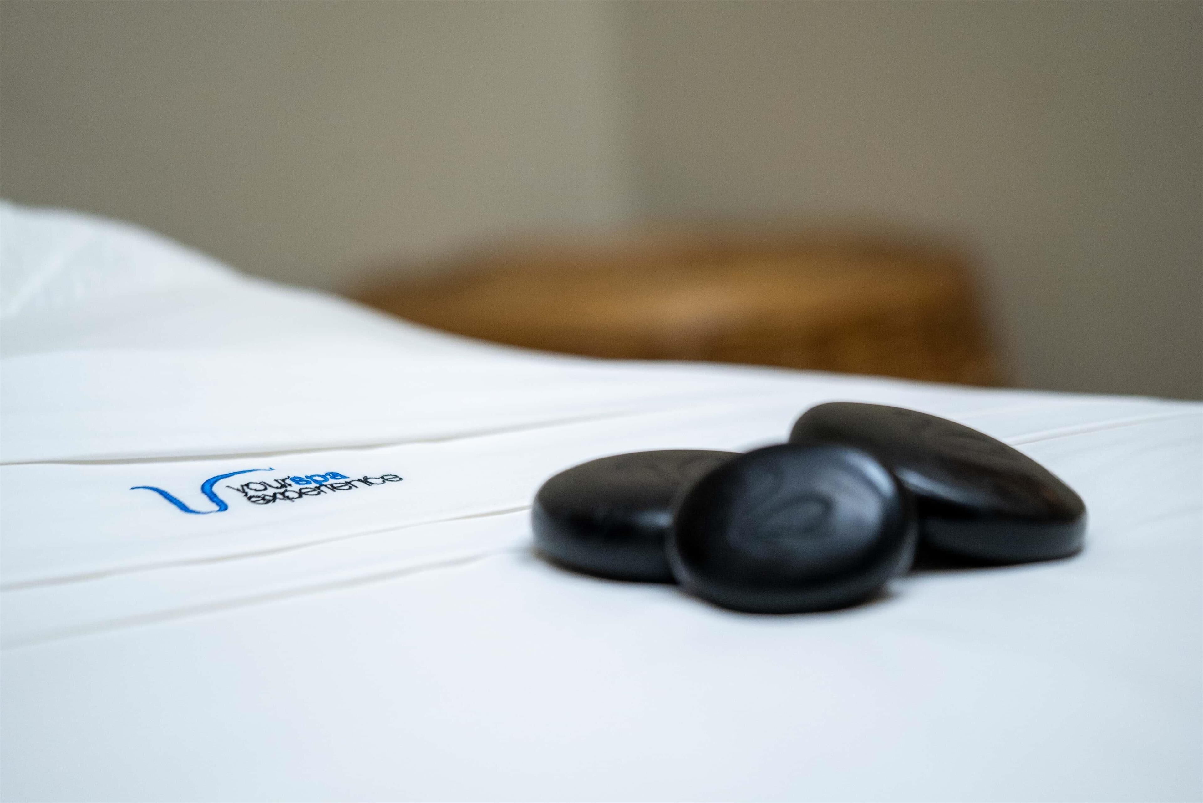 A massage table with black stones and a logo on the white sheet.