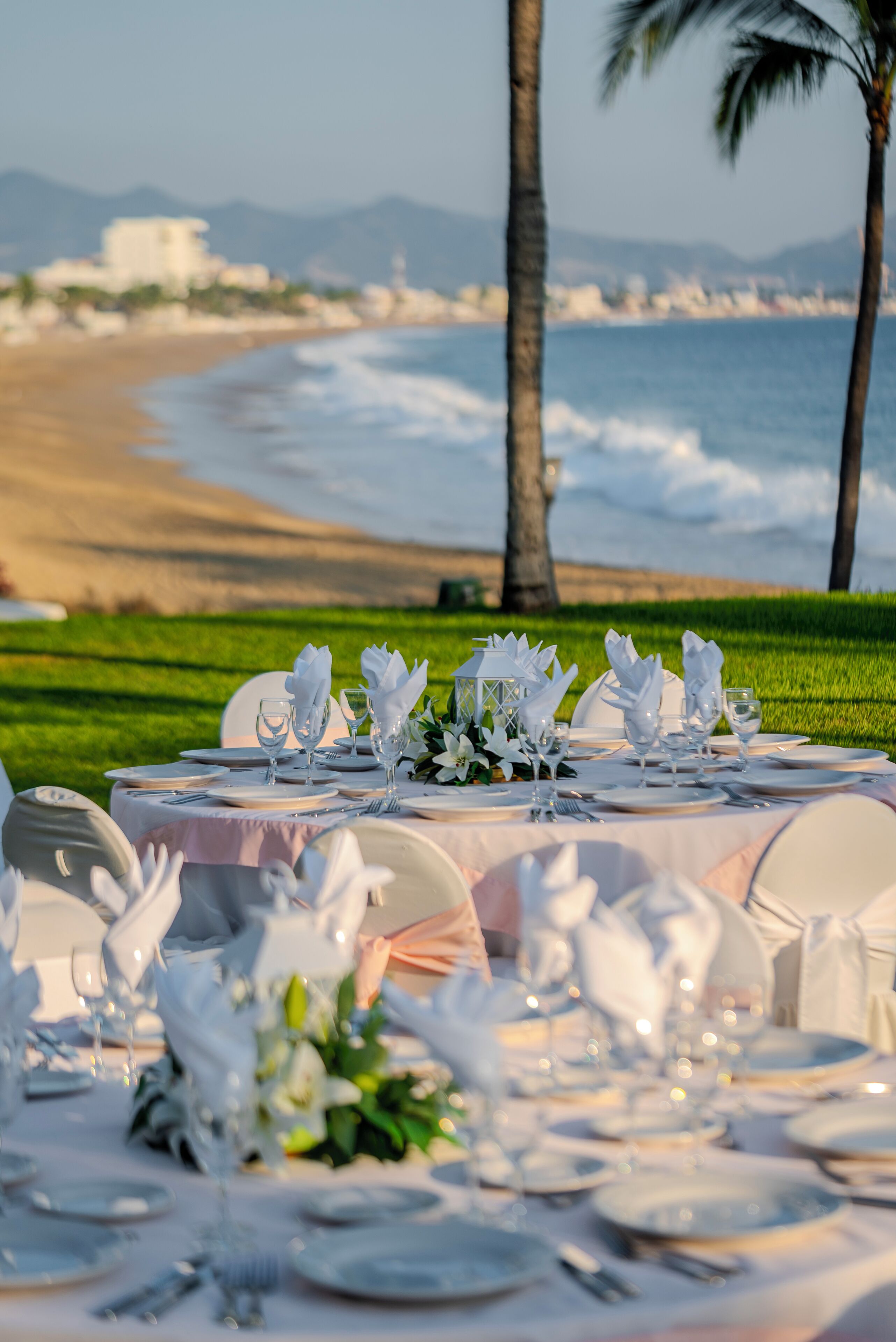 A table set for a formal outdoor event with a view of the ocean and palm trees.