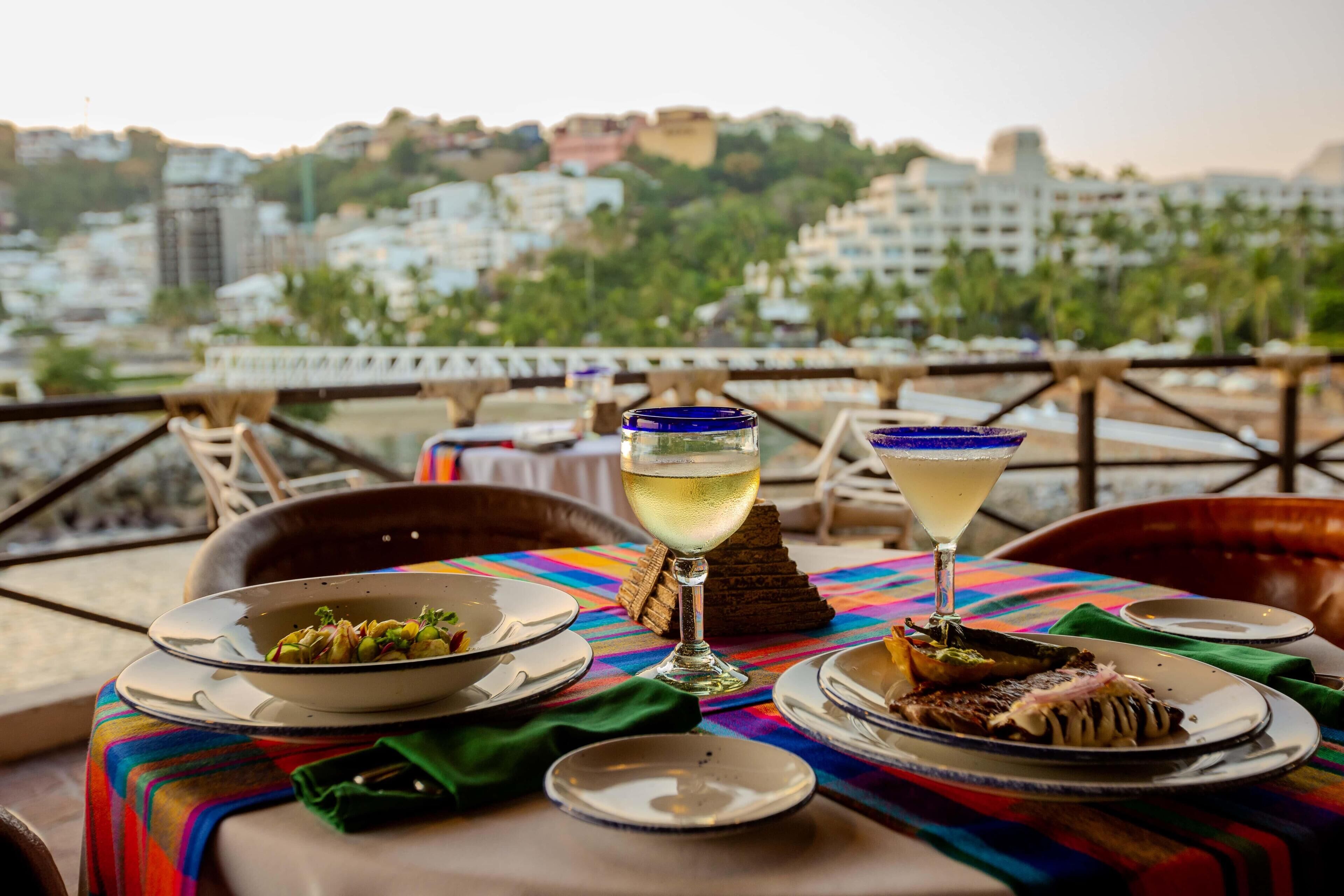 A table set with plates of food, two glasses of a clear beverage, and a colorful tablecloth.