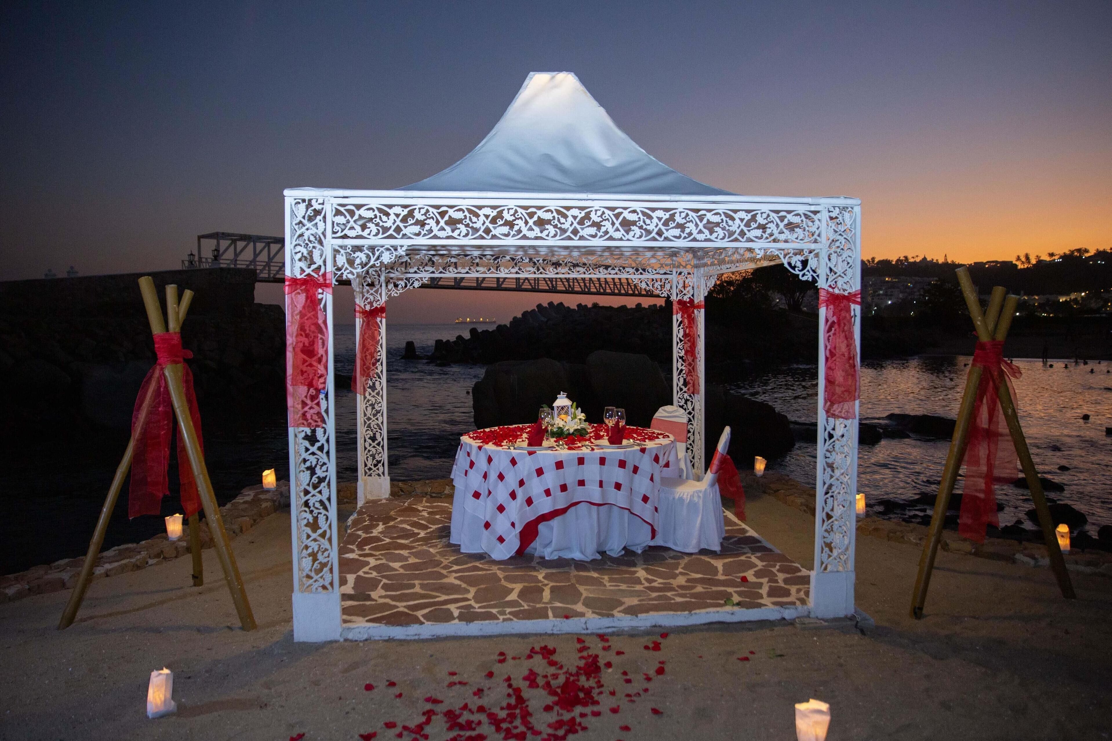 A beachside wedding setup with a white canopy and a table adorned with flowers and candles.