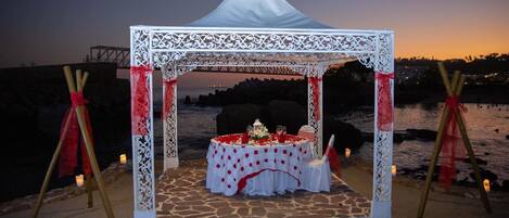 A beachside wedding setup with a white canopy and a table adorned with flowers and candles.