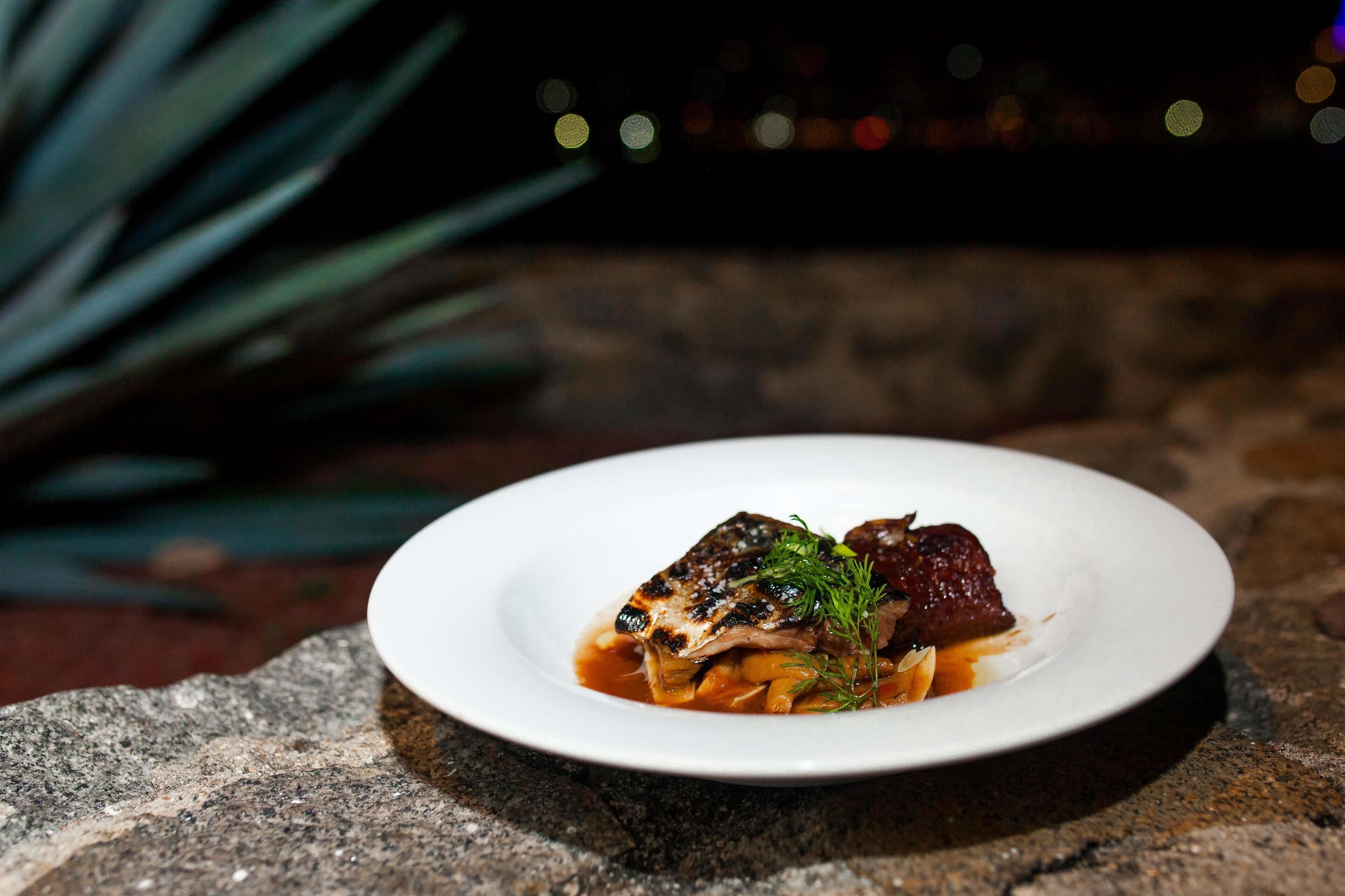 A white plate with a dish of food on a stone surface.