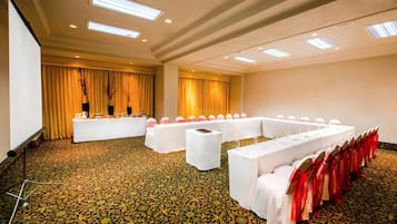 Un salón de conferencias con una larga mesa, manteles blancos y cintas rojas.