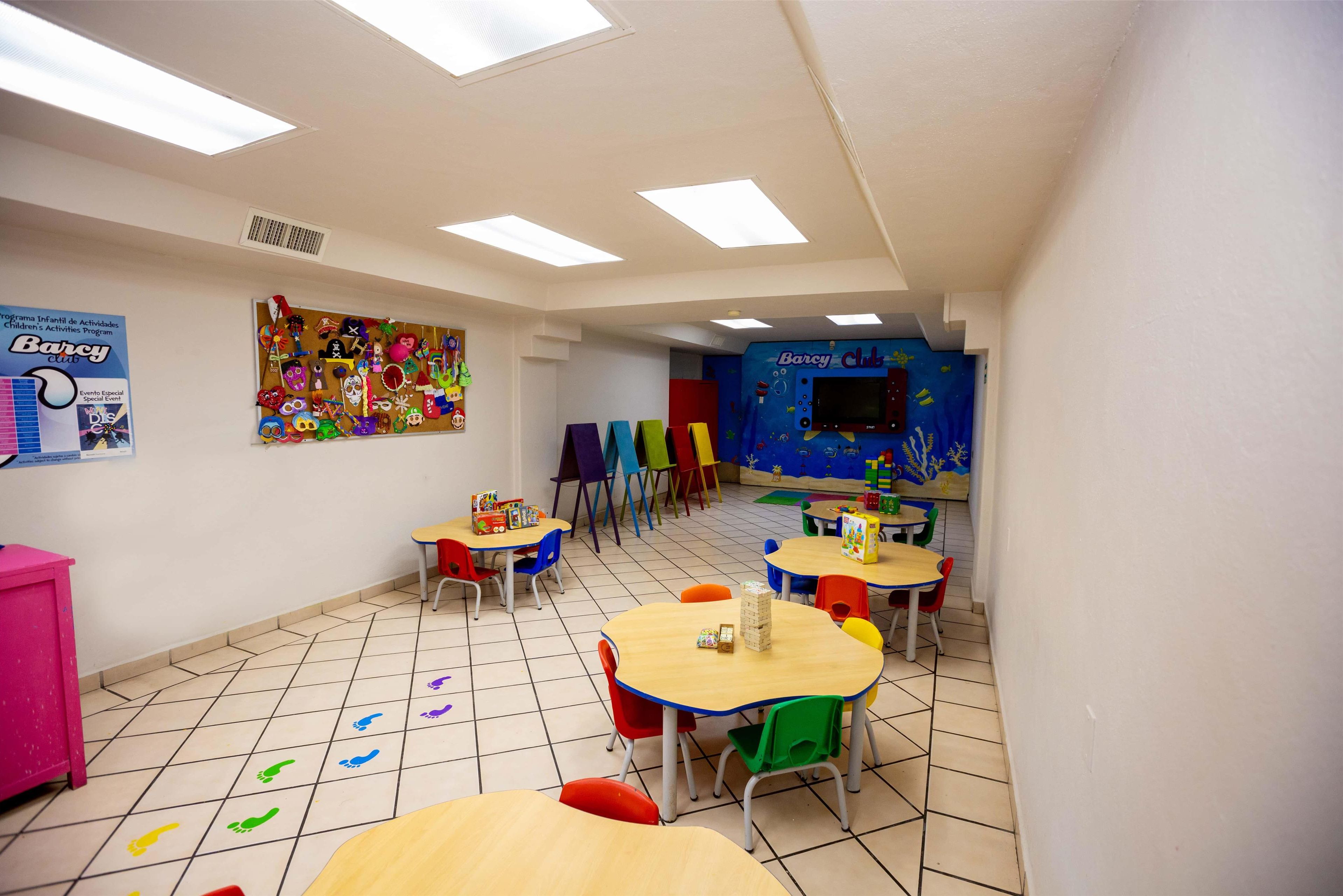 Un aula con sillas y mesas coloridas, y carteles educativos en las paredes.