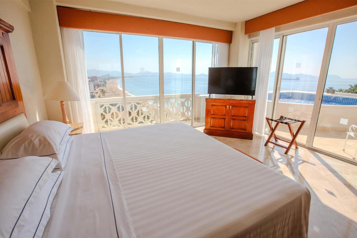 Quarto de hotel com uma cama grande, televisão e varanda com vista para o mar.