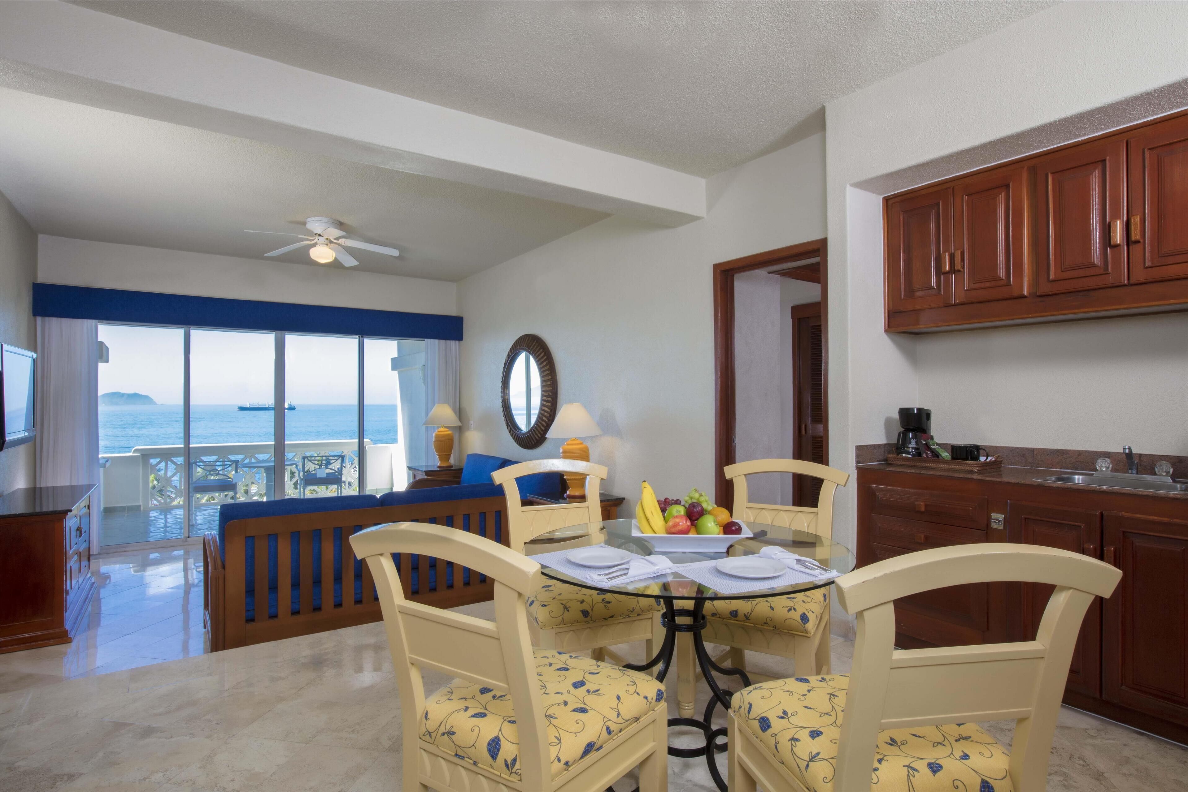 Un'area pranzo con tavolo imbandito per quattro persone, vista mare e cucina con mobili in legno.