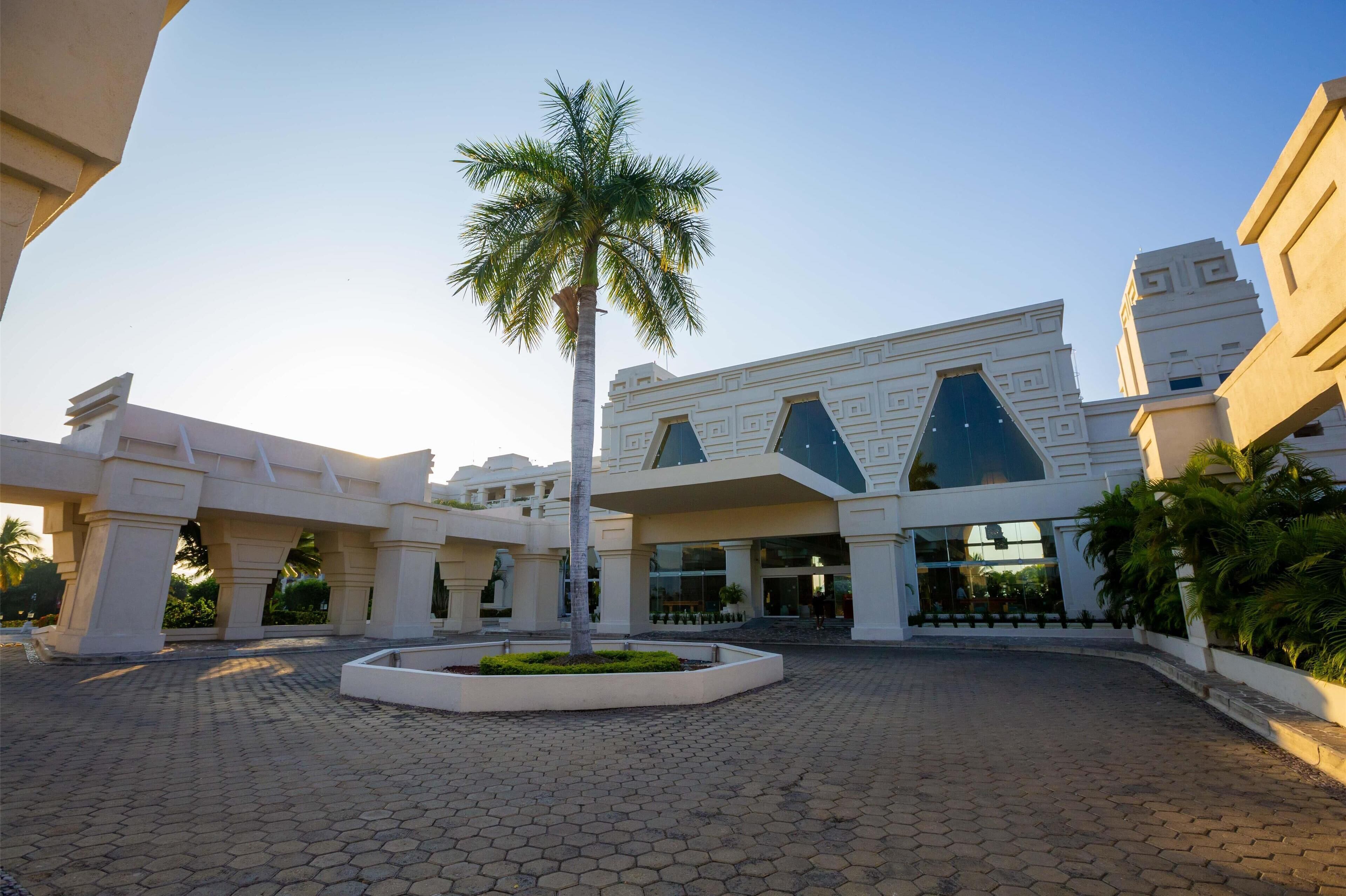 A modern building with a central atrium, palm trees, and a paved courtyard.