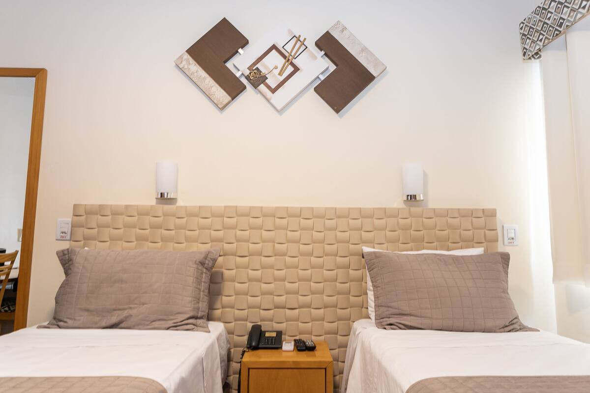 A hotel room with two beds, a wooden nightstand, a phone, and a wall-mounted light fixture.