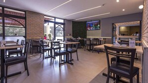A modern restaurant with multiple tables and chairs, a TV screen on the wall, and a brick accent wall. - Hotel Marbor (Mogi das Cruzes)