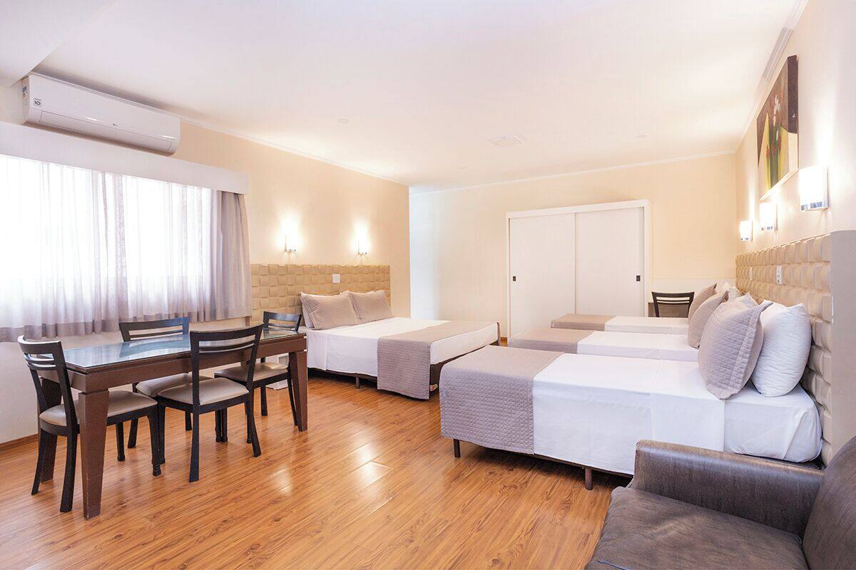 A hotel room with a wooden dining table, two single beds, a sofa, and a built-in wardrobe.