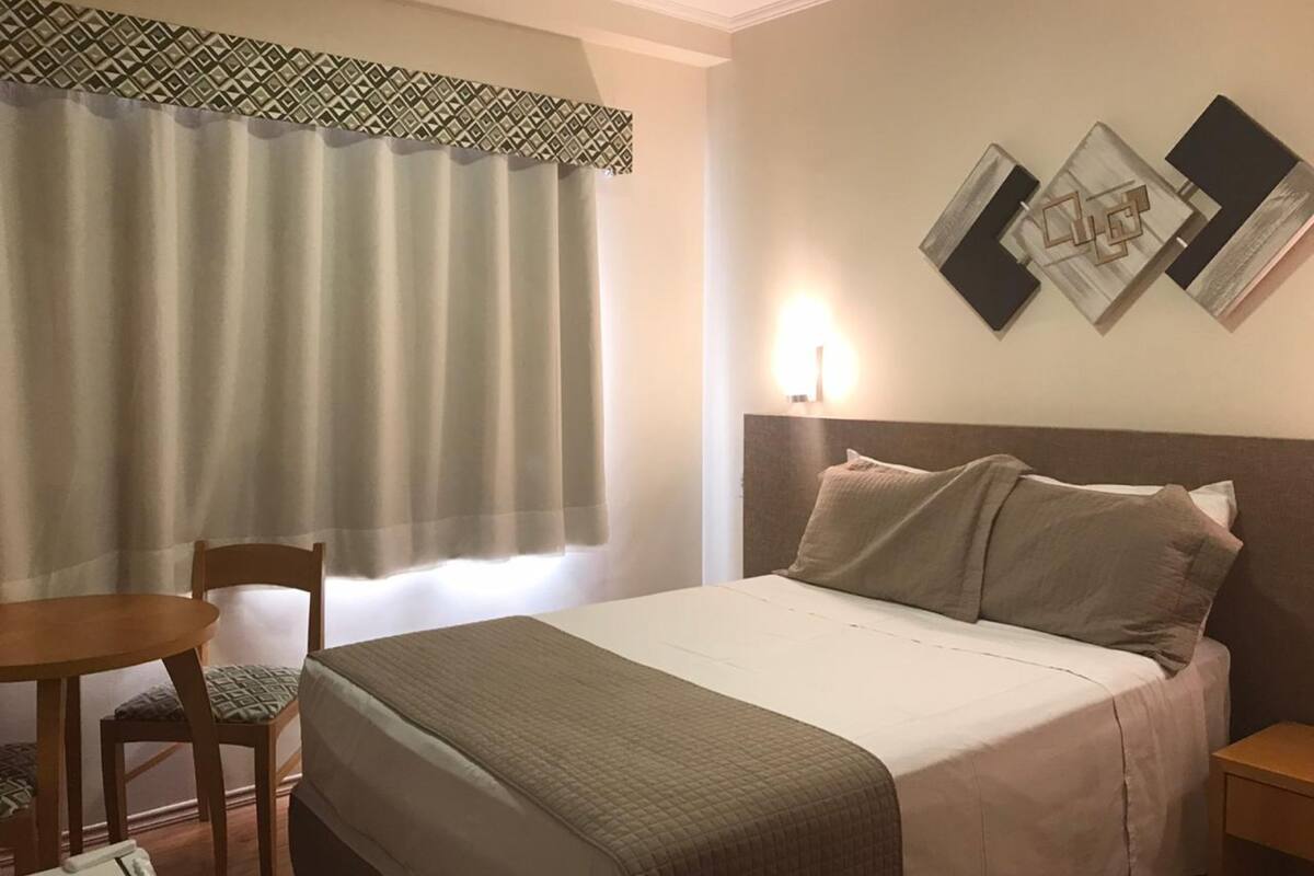 A hotel room with a bed, a chair, a table, and a wall-mounted light.