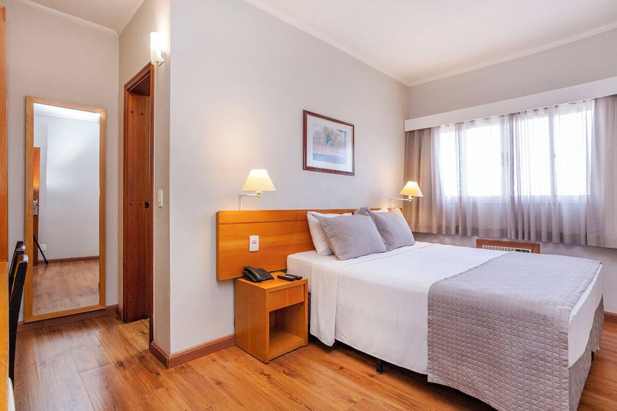 A hotel room with a large bed, bedside lamps, a nightstand, a framed picture on the wall, and a window with curtains.