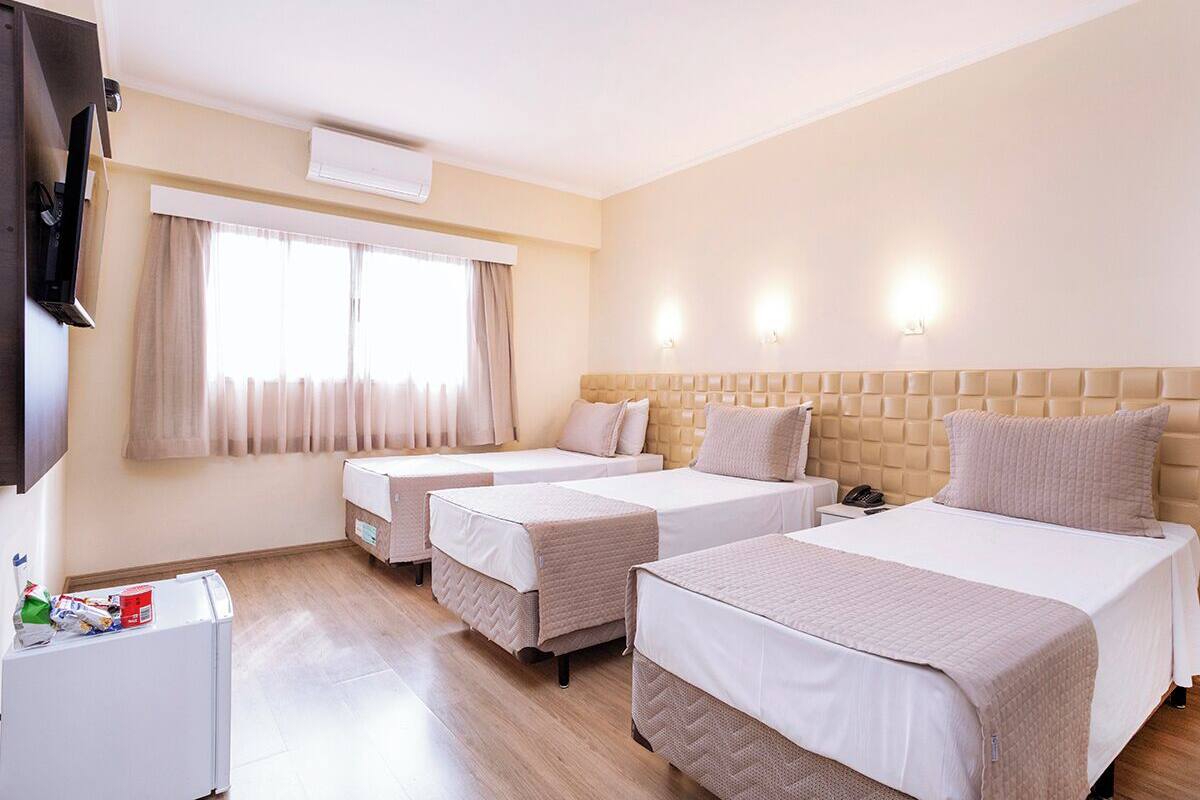 A hotel room with three beds, a television, a refrigerator, and a window with curtains.