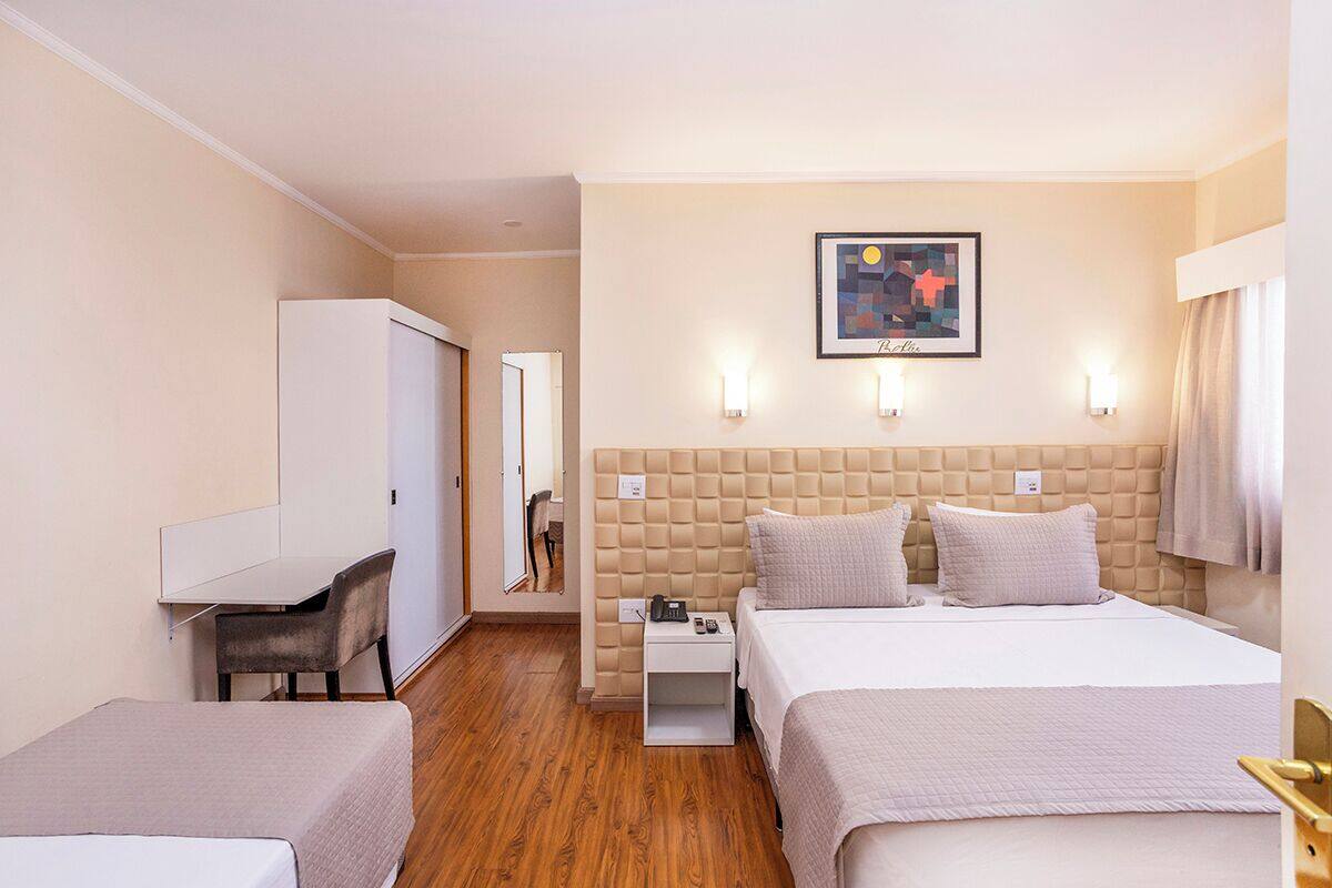 A hotel room with a large bed, a desk, a chair, and a wardrobe.