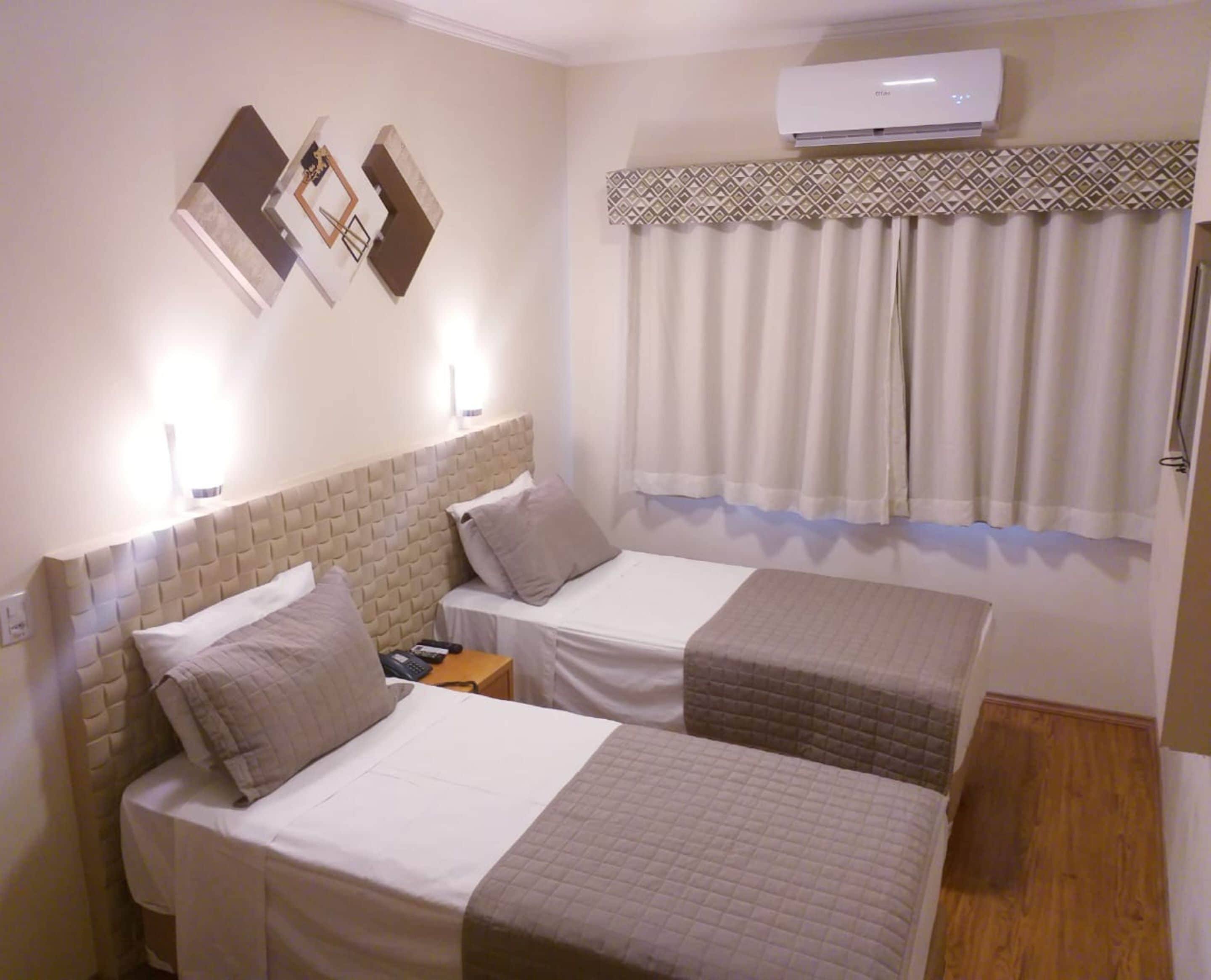 A hotel room with two single beds, a wall-mounted air conditioner, and a patterned curtain.