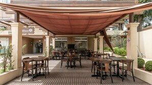 A covered outdoor seating area with tables and chairs, a sign for 'Hotel Marbor', and a brick building in the background. - Hotel Marbor (Mogi das Cruzes)