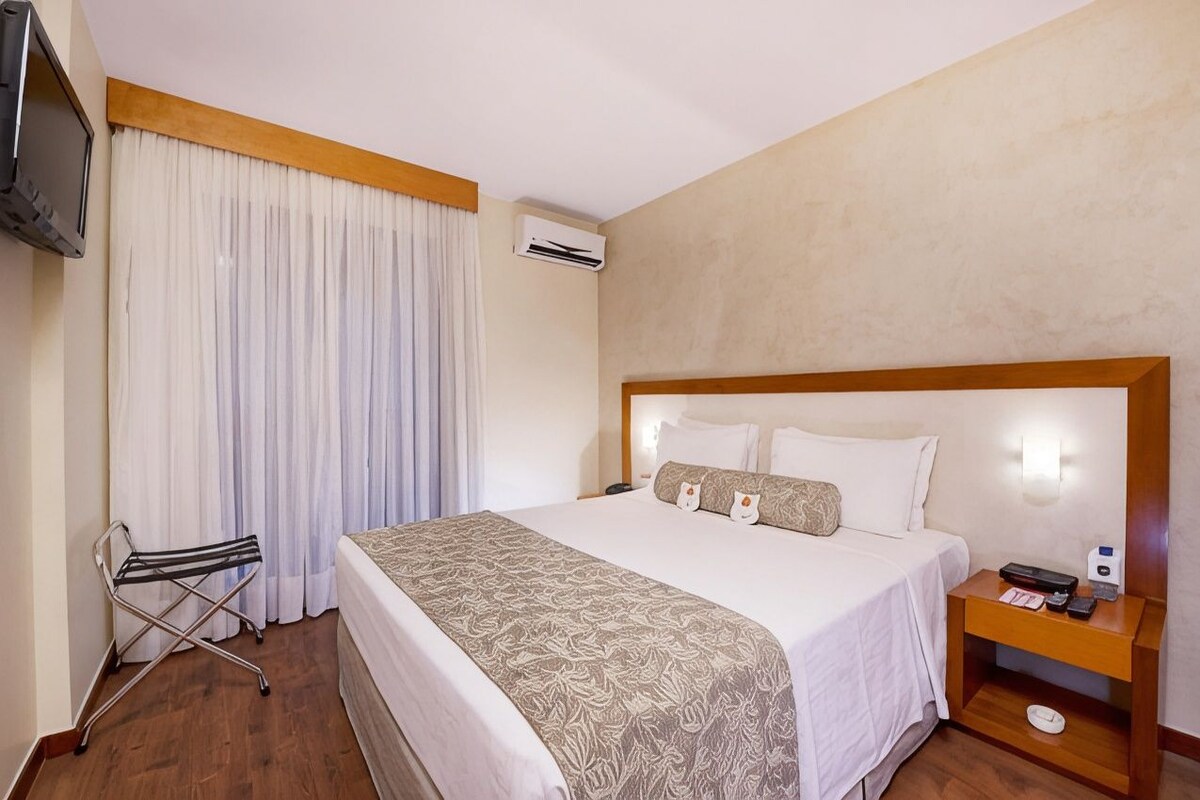 Una habitación de hotel con cama, mesita de noche, silla, televisor y aire acondicionado.