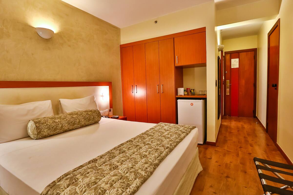 A hotel room with a bed, wooden wardrobe, a small kitchenette, and a hallway.