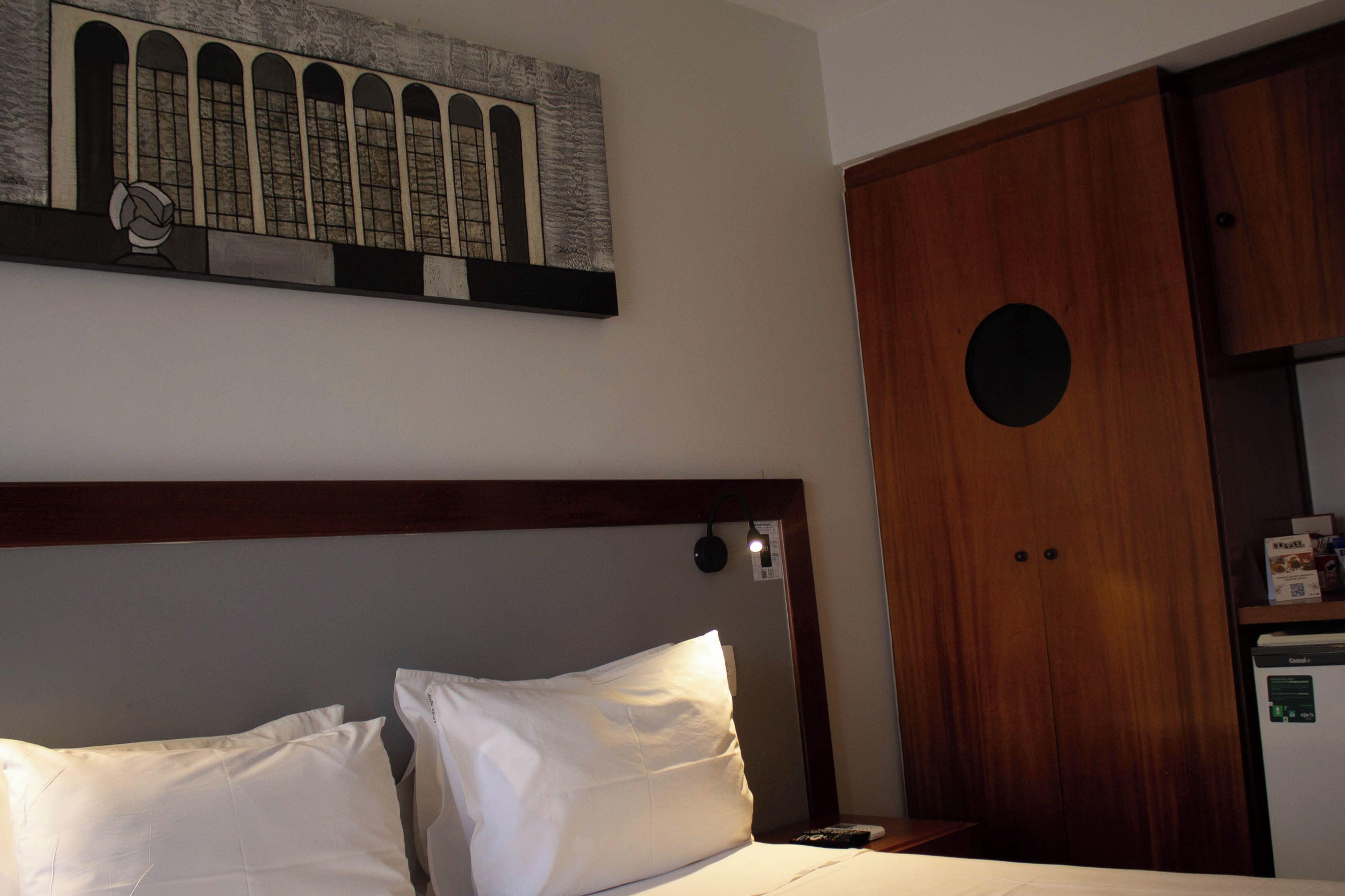 Una habitación de hotel con una cama, un armario de madera y una obra de arte colgada en la pared.