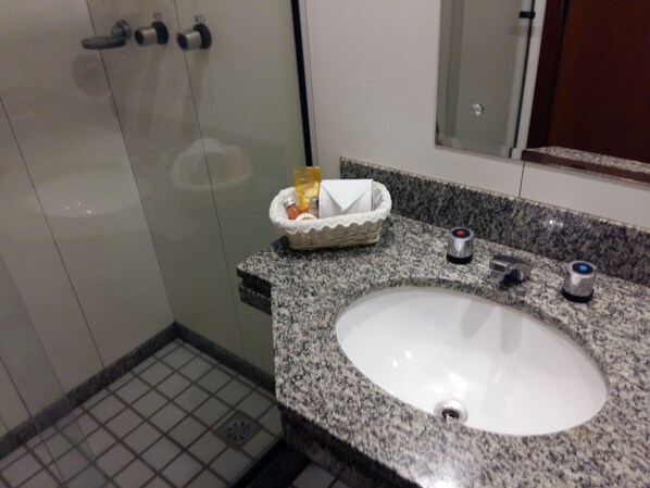 Un baño con encimera de granito, un lavamanos blanco y cabina de ducha con mampara de vidrio.