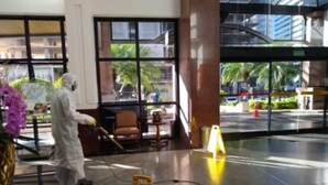 Une personne, vêtue d’un  équipement de protection, nettoie un hall d’entrée à l’aide d’un vaporisateur.