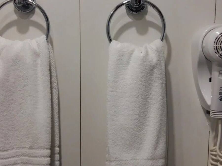 Dos toallas blancas colgadas en aros metálicos, y un secador de pelo blanco sobre una pared.