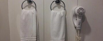 Duas toalhas brancas penduradas em argolas de metal, e um secador de cabelo branco fixado na parede.