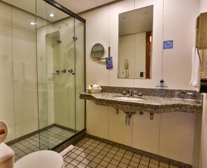 Un baño con ducha envuelta en vidrio, lavamanos con encimera de granito y un espejo.
