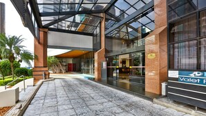 Une entrée moderne avec une façade en verre, un panneau indiquant un service de voiturier et un trottoir dallé.