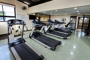 Un gimnasio con varias cintas de correr, un televisor en la pared y un letrero que indica la salida.