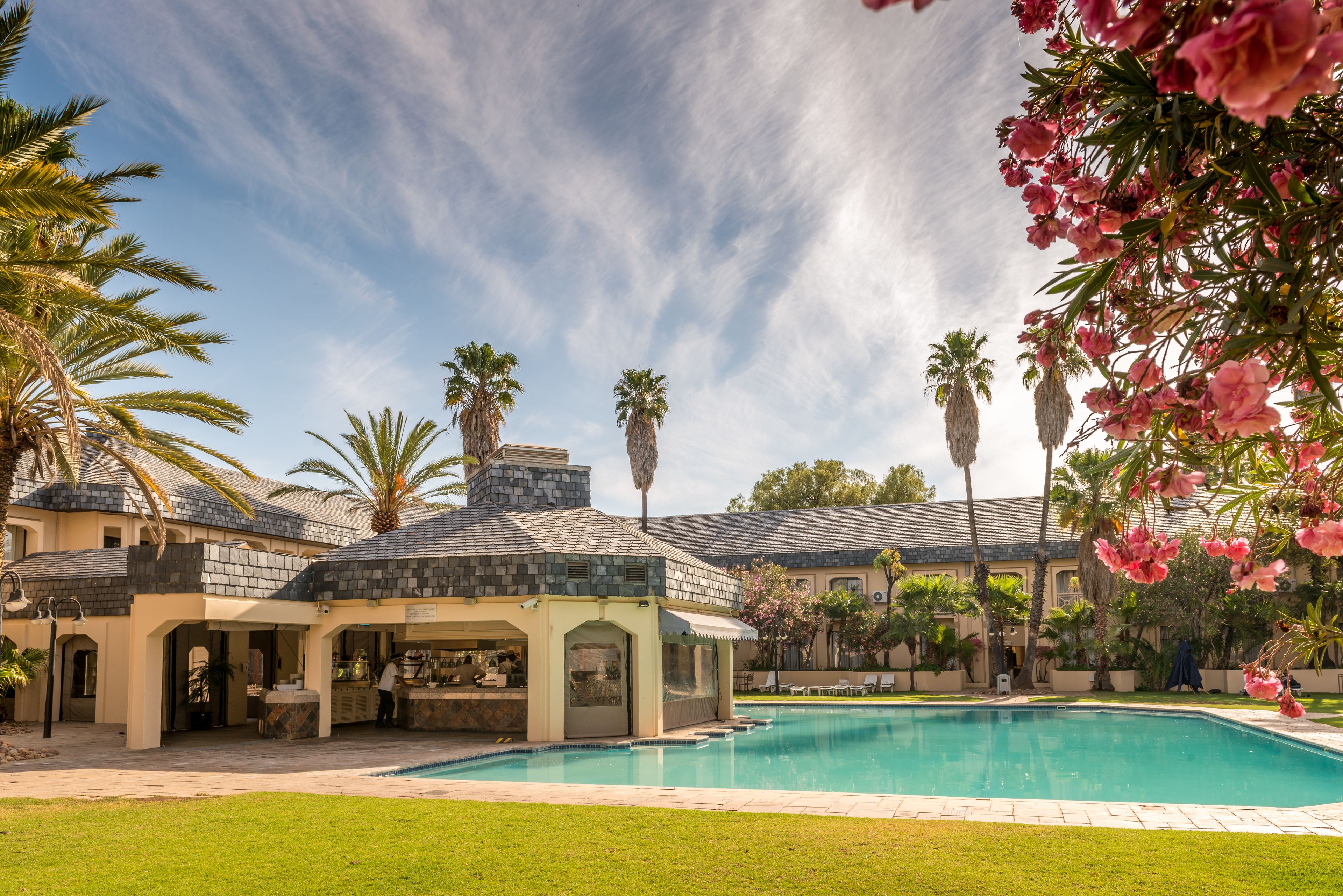 A pool area with a covered seating area, palm trees, and a building with a stone facade.