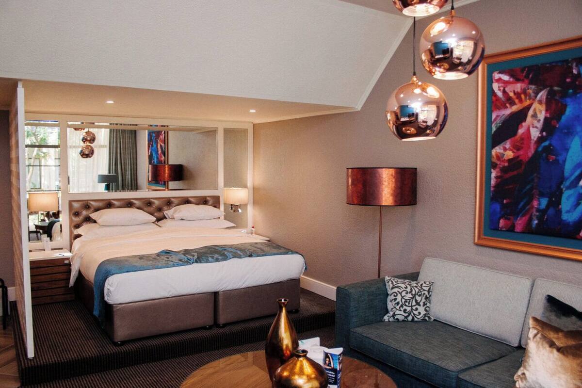 A hotel room with a large bed, a sofa, a coffee table, and a painting on the wall.