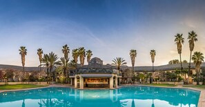 Ein Poolbereich mit Bar und Lounge, umgeben von Palmen und einem Gebäude mit einem Ziegeldach.