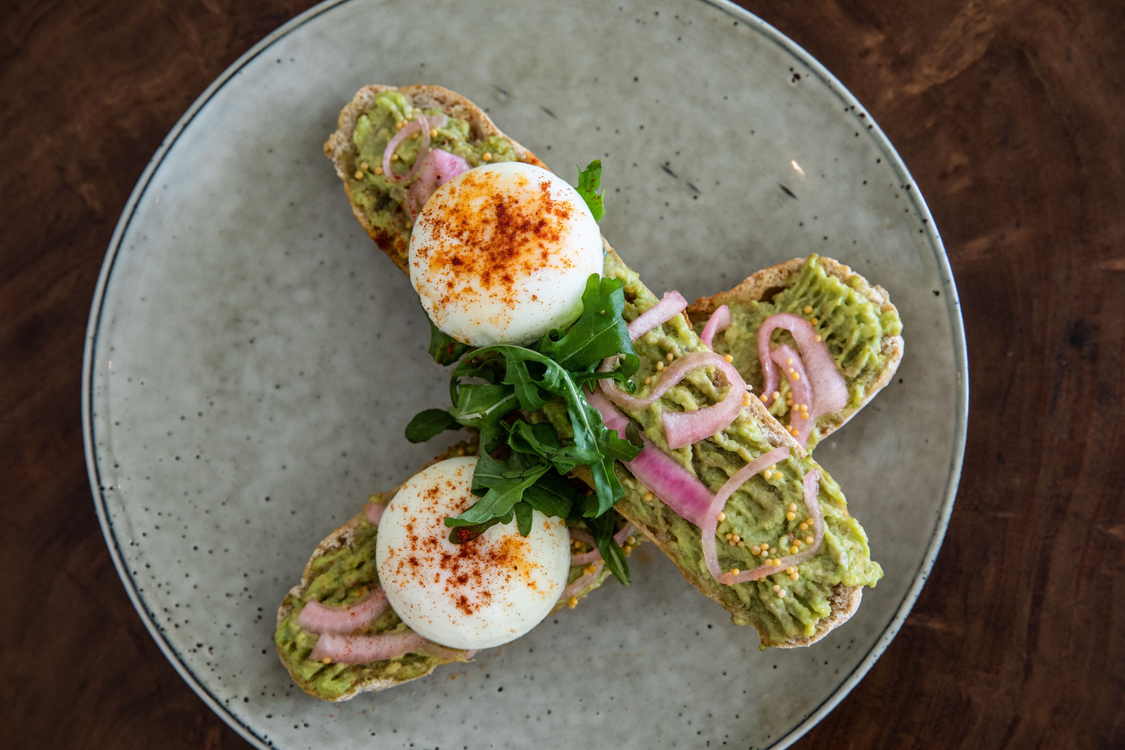 A plate with a sandwich topped with avocado, egg, and greens.