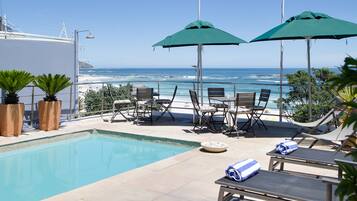 Ein Poolbereich mit Liegestühlen, Sonnenschirmen und Blick auf das Meer.
