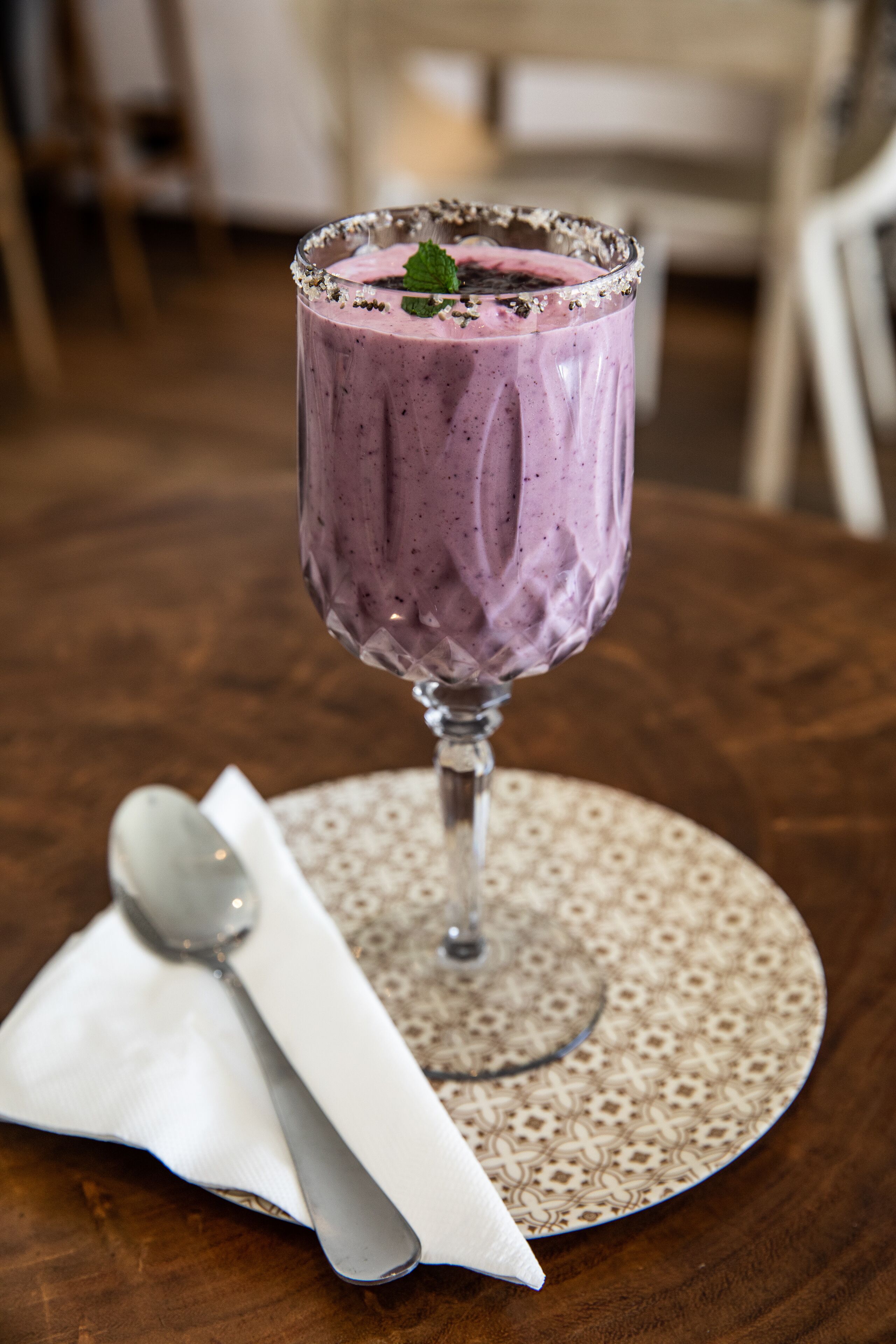 Un verre de smoothie violet, posé sur un dessous de verre à motifs, avec une cuillère et une serviette à côté.