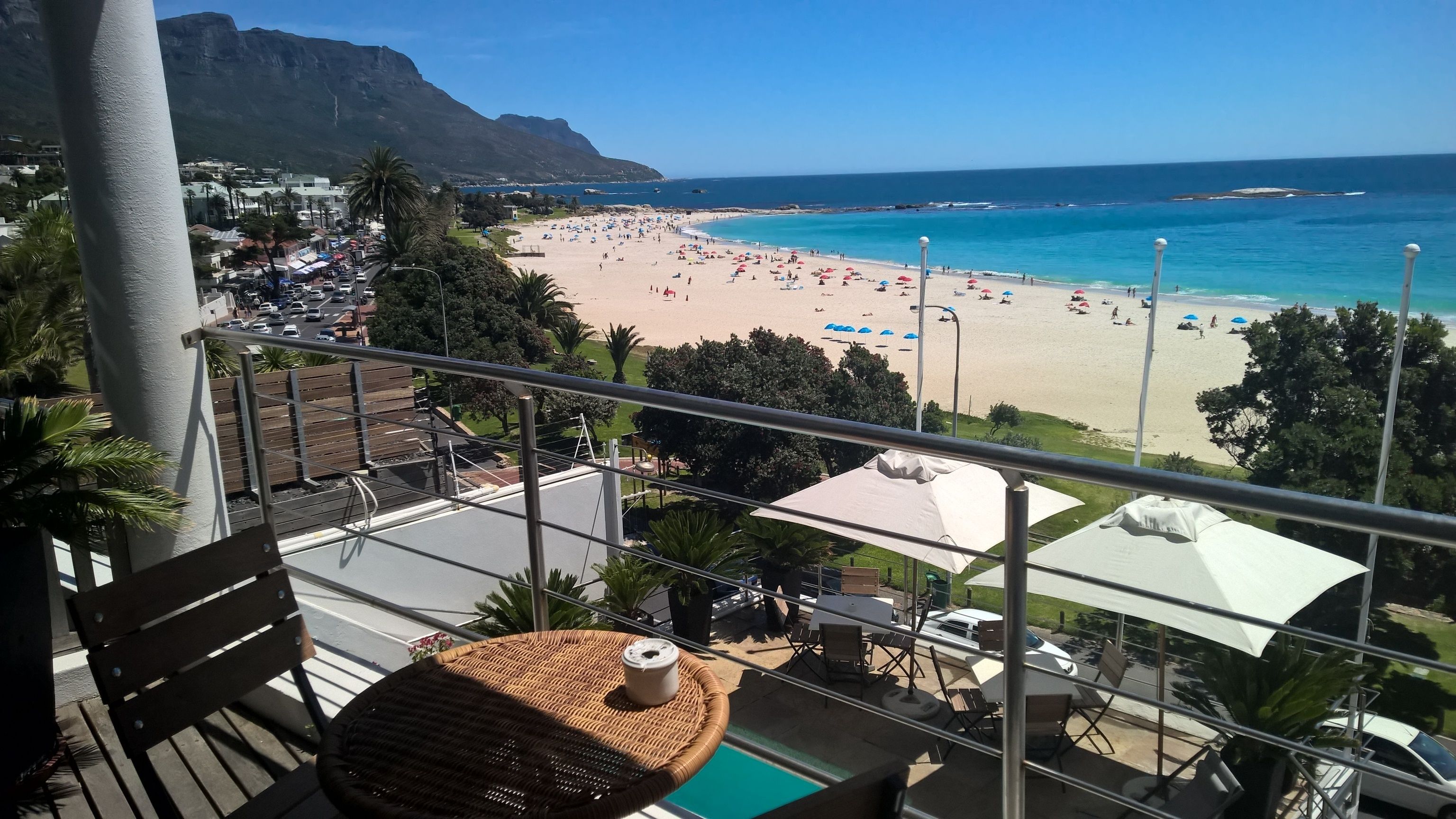 A balcony with a view of a beach, a pool, and a mountain in the background.
