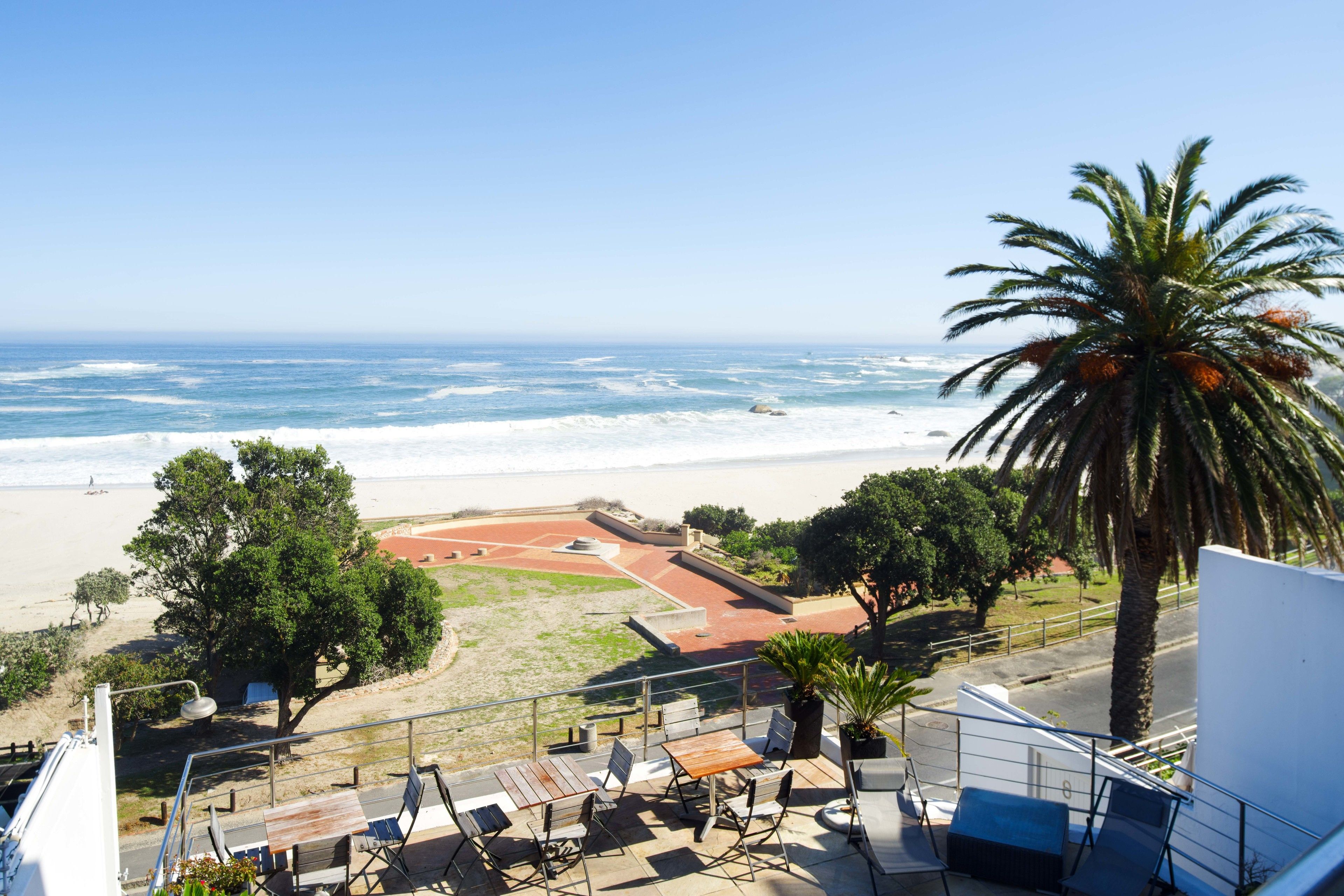 A balcony with outdoor seating overlooking a beach and ocean.