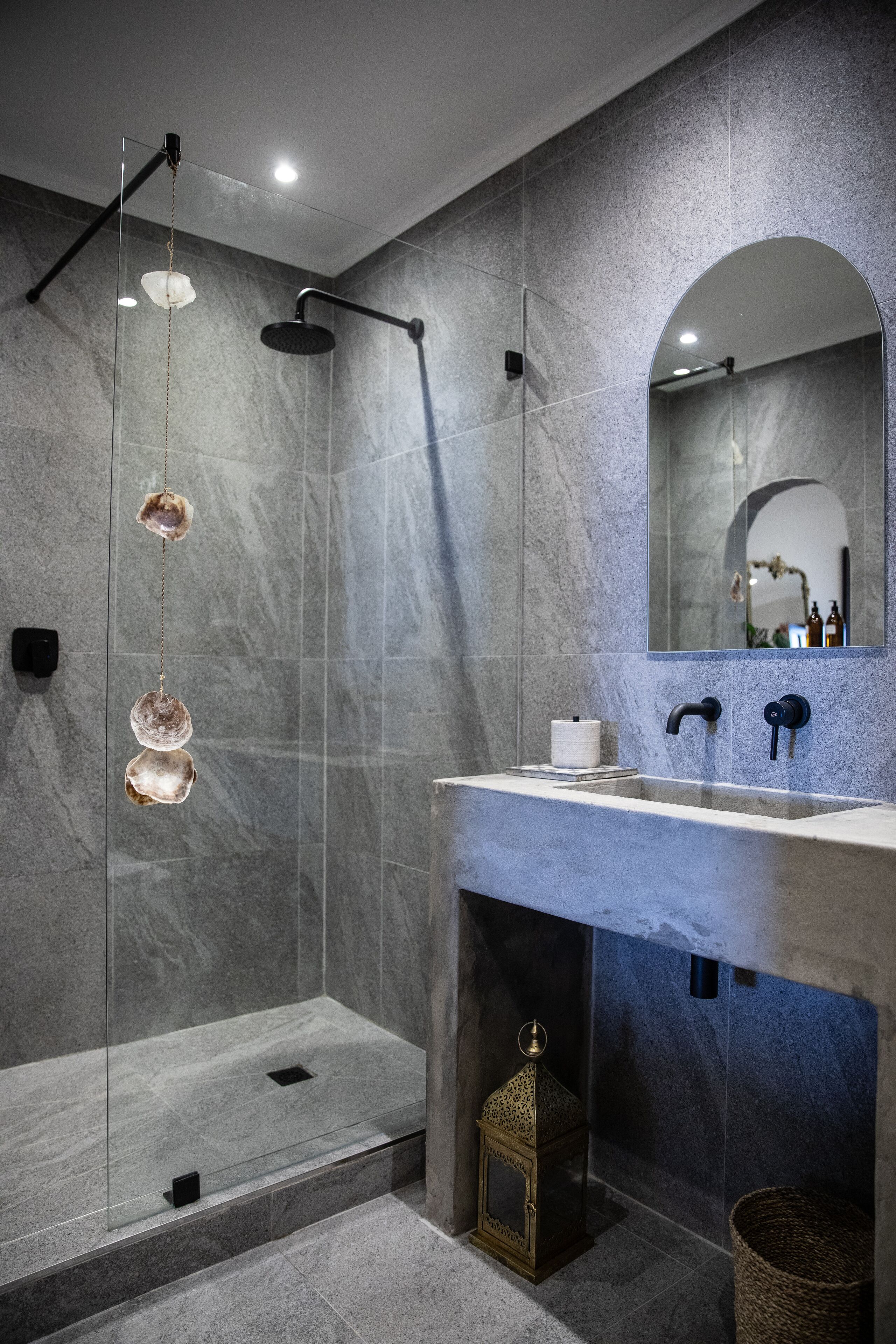 A modern bathroom with a glass-enclosed shower, a marble-tiled wall, a sink with a mirror, and a small decorative lantern.
