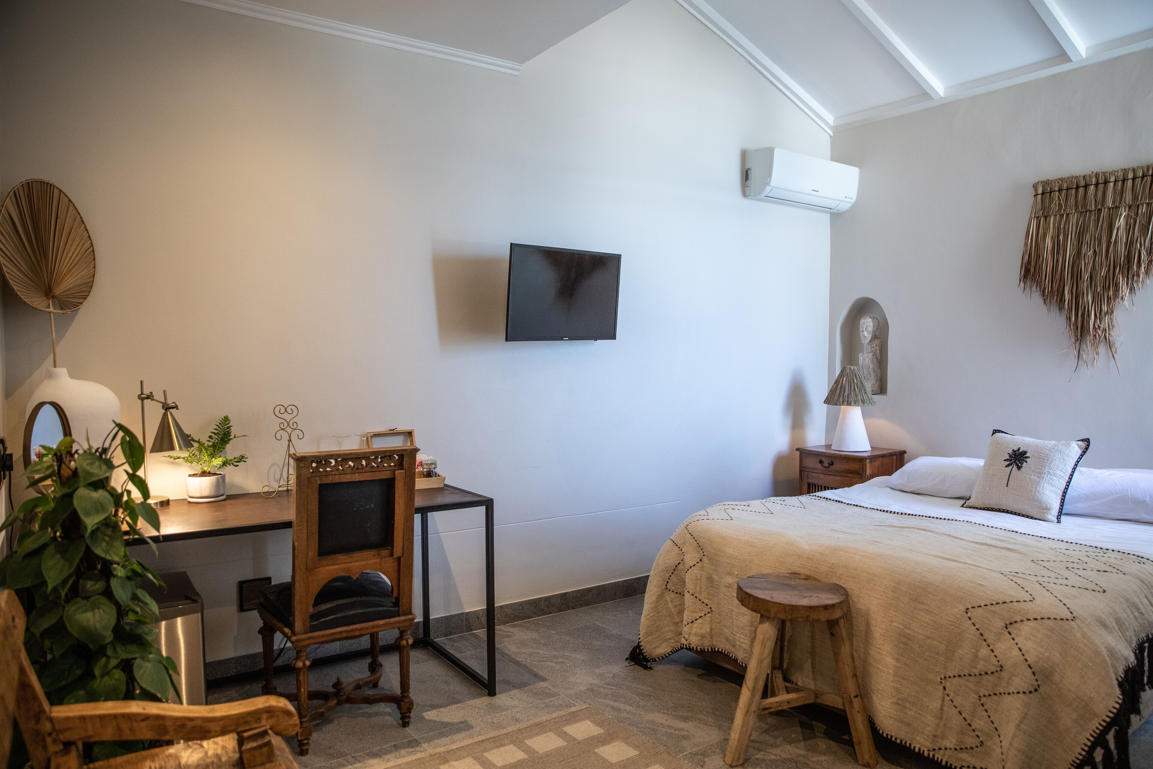 A bedroom with a bed, a desk with a chair, a television, and a small table.