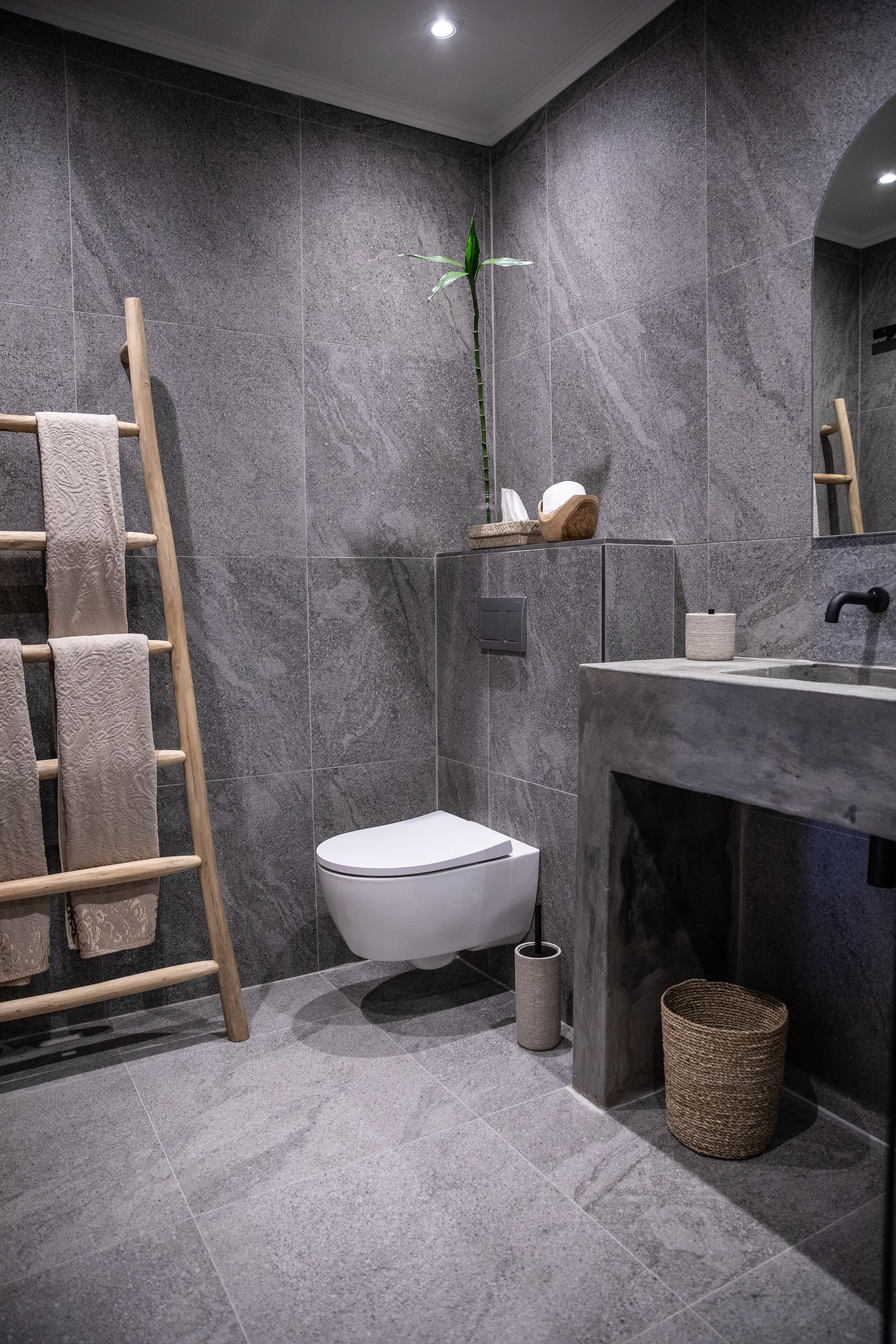 Une salle de bain moderne avec des toilettes blanches, un porte-serviettes en bois, un grand miroir et un mur en pierre.