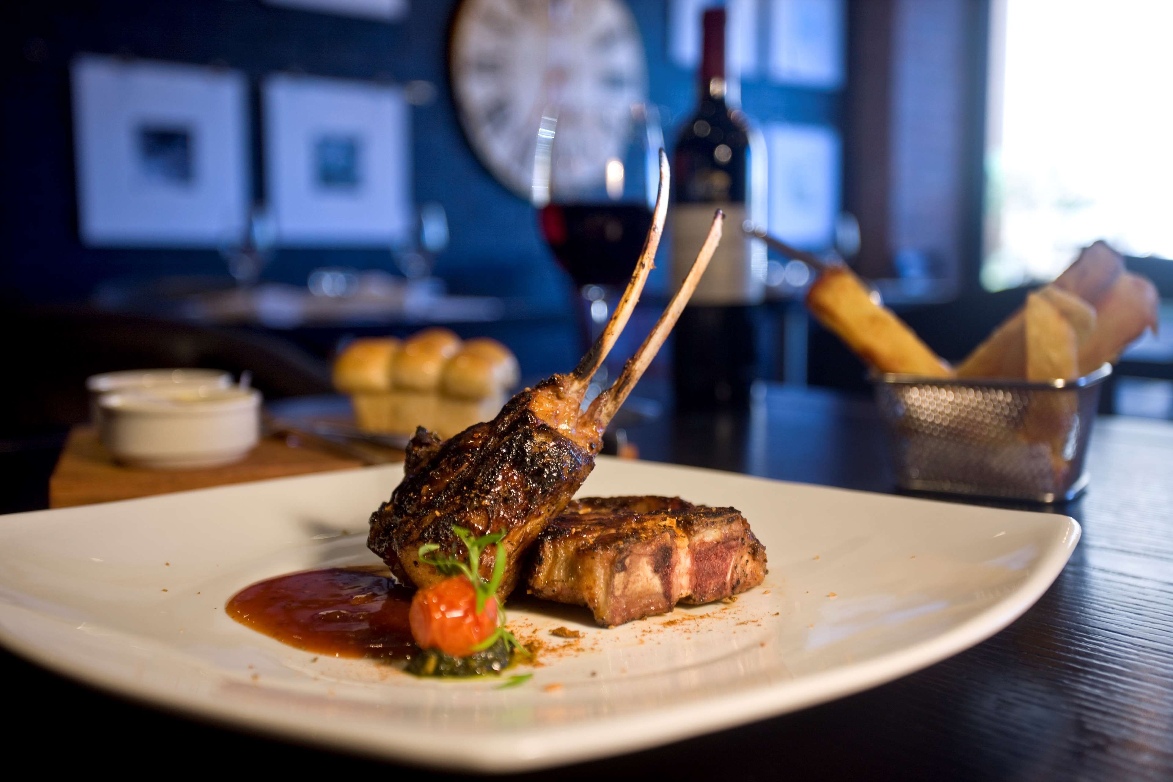 Une assiette avec une côtelette d’agneau grillée et une portion de sauce à part.